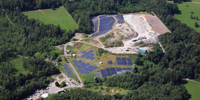 Letecký pohled na skládku odpadů, kde je vidět několik etap, včetně zrekultivovaných ploch osazených fotovoltaickými panely.