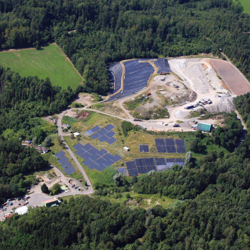 Letecký pohled na skládku odpadů, kde je vidět několik etap, včetně zrekultivovaných ploch osazených fotovoltaickými panely.
